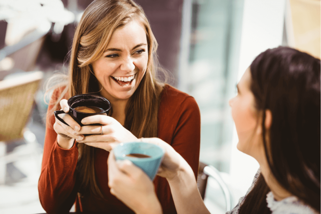 Two women laughing and talking whilst drinking coffee