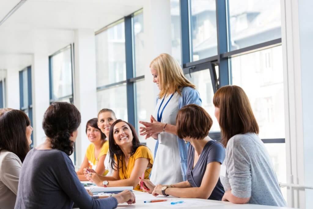 A woman presenting a workplace wellbeing workshop to a group of employees sat around a meeting table